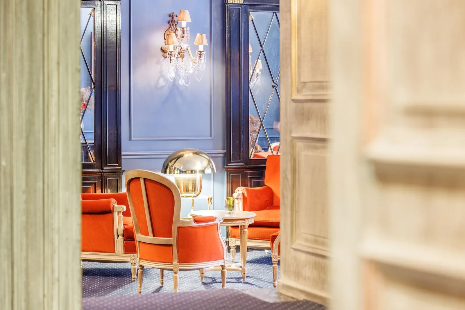 Lounge at The Black Swan Hotel with orange armchairs, a marble side table and a crystal wall sconce against blue panelling